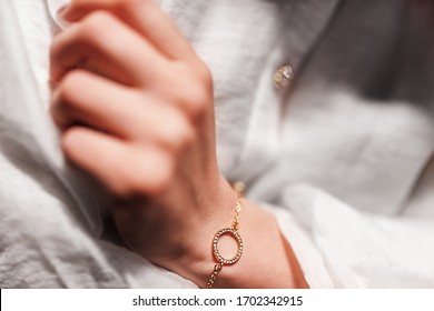 gold bracelet in the form of a ring with diamonds on a chain, girl’s hand, sleeve of a white shirt, dark background.