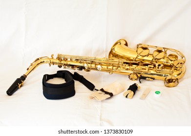 A Gold / Brass Alto Saxophone On White Background With Pearl Keys - Laid Out With Accessories Including Strap, Cleaner, Reed And Cork Grease