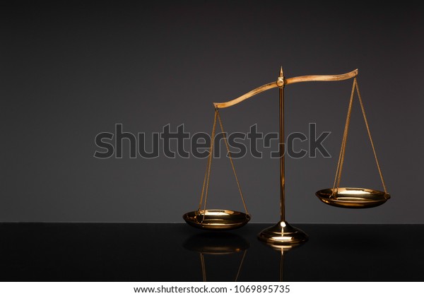 Gold\
brass balance scale, weight balance, imbalance scale with\
reflection on glass desktop with black\
background.