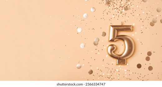 Gold candle in the form of number five on peach background with confetti.