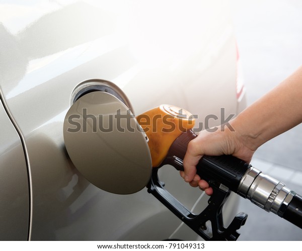 The gold car is filling the fuel at\
the oil station. Hand holding Fuel nozzle in gas\
pump.
