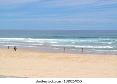 Gold Coast Australia, January 2019: Danger Sign And Red Flag On The Beach With People In Sea And Walking On Sand.