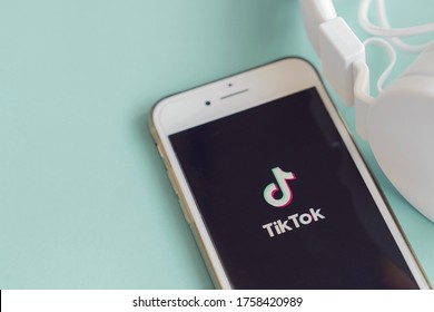 Gold Coast, Australia - June 17, 2020 : Smartphone With Tik Tok App On Screen And White Headphone On Blue Background