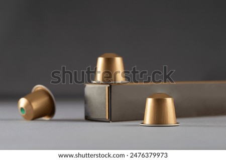 Gold coffee capsules arranged near a box on a gradient background, modern packaging