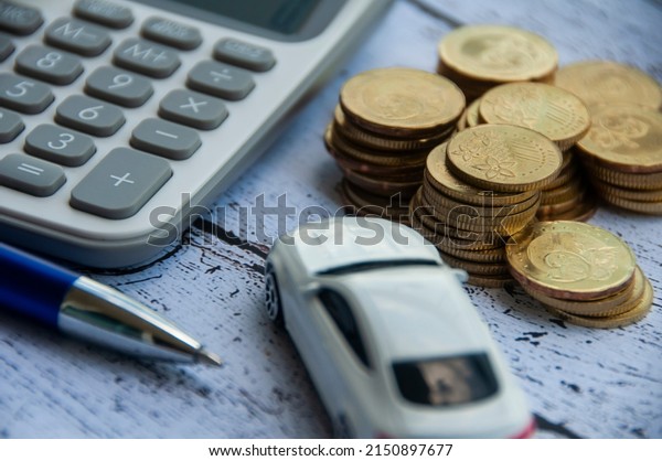 Gold coins, calculator, white car toy and pen on\
wooden background. Selective focus on coins. Finance and copy space\
concept