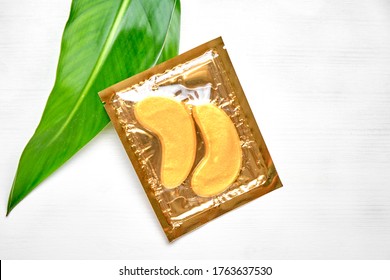 Gold Collagen Eye Mask Or Patches On A White Background With Green Leaves. Skin Care And Beauty Concept. 