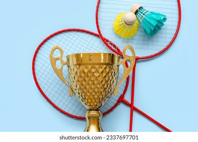 Gold cup with badminton rackets and shuttlecocks on blue background