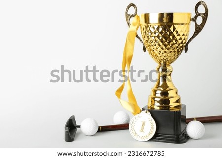 Gold cup with first place medal, golf club and balls on light background