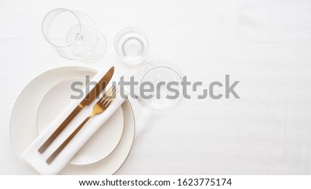 Gold cutlery knife and fork  in porcelain plate and wine glass on white tablecloth  for restaurant dinner concept.