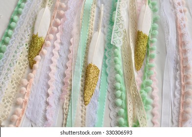 Gold Dipped Glitter Goose Feathers Laying On Pink Peach Mint Blue Laces Vintage Ribbons And Pom Pom Trimming