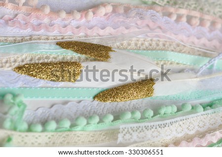 Gold Dipped Glitter Goose Feathers Laying On Pink Peach Mint Blue Laces Vintage Ribbons And Pom Gold Dipped Glitter Goose Feathers Laying On Pink Peach Mint Blue Laces Vintage Ribbons And Pom