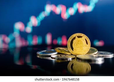 Gold Dogecoin and other crypto coins on reflecting table. Blurred candlestick chart in the background. DOGE is the most popular meme coin in cryptocurrency world.
