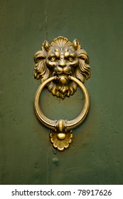 A gold doorknocker in the shape of a ferocious lion is mounted on a green door