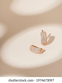 Gold earrings with diamonds on soft beige background. Still life and creative photo with shadows.