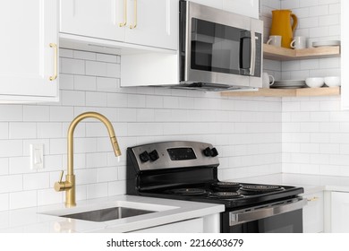 A Gold Faucet Detail Shot In A White Kitchen, Subway Tile Backsplash, And Stainless Steel Appliances.