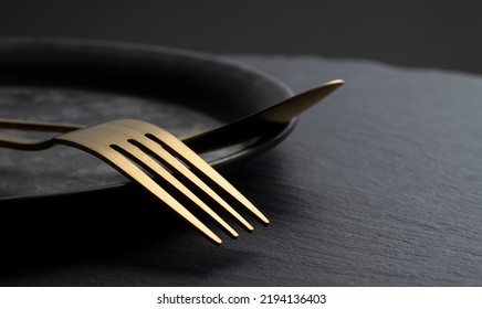 Gold Fork And Spoon Placed On A Black Iron Plate. Beautiful Gold Cutlery.