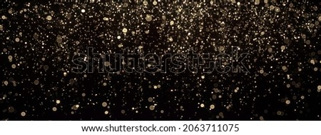 Gold glitter texture on black. Shinny small particles reflecting light. Defocused abstract background.