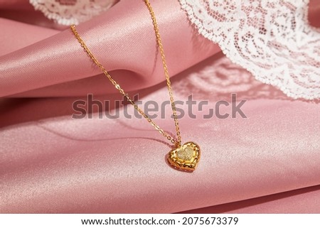 gold heart at chain, isolated on pink silk background, jewelry display