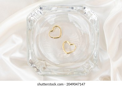 Gold Heart Shaped Earrings In An Ashtray On A White Fabric