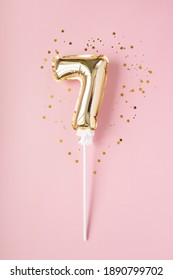 Gold inflatable number 7 on a stick with gold confetti on a pink background.