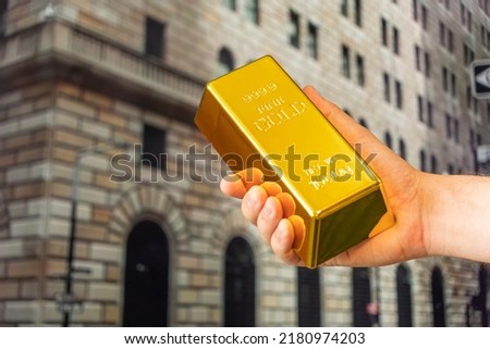 gold ingot in hand on background Federal Reserve Bank of New York. The building hosts a vault containing the world's largest depository of gold. outside