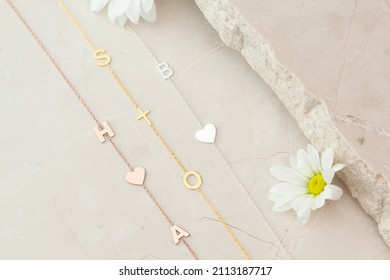 Gold Initial Necklaces With Daisies And On A Marble Floor. Personalized Necklace Image. Jewelry Photo For E-commerce, Online Sale, Social Media.