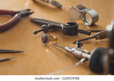 Gold jewelry production concept. Luxury golden ring with ruby gemstone on jeweler's workbench. Workplace of a jeweler. Tools and equipment for jewelry work on an antique wooden desktop. - Powered by Shutterstock