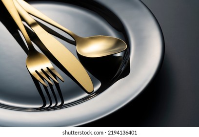 Gold knives, forks and spoons on black plates. Beautiful gold cutlery. Clos