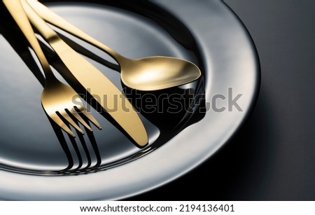 Gold knives, forks and spoons on black plates. Beautiful gold cutlery. Clos