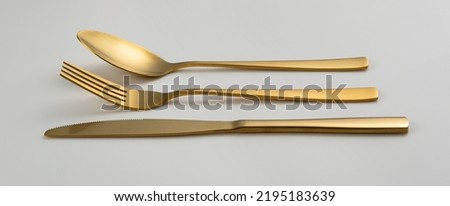 Gold knives, forks and spoons placed on a white background. Beautiful gold cutlery. View from the side.