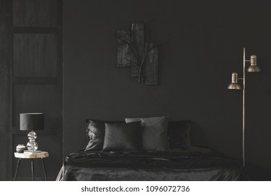 Gold lamp next to bed in black bedroom interior with sculpture on dark wall