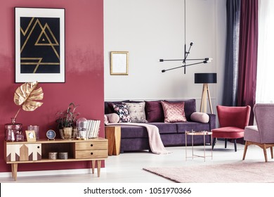 Gold Leaf On Wooden Cupboard Against Red Wall With Black Poster In Spacious Living Room Interior