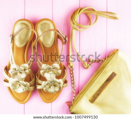 gold leather women's sandals with a gold handbag decorated with flowers on a pink background