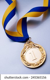 Gold Medal In The Foreground On Yellow Blue Ribbon