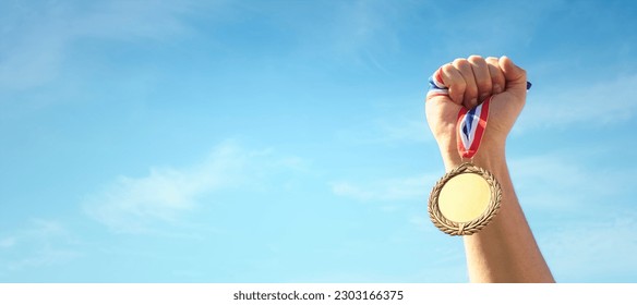 Gold medal winner held in athlete hand raised against blue sky background concept for winning, success and victory - Powered by Shutterstock