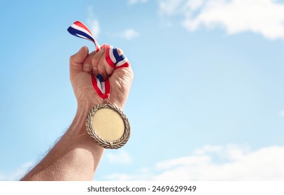 Gold medal winner held in athlete hand raised against blue sky background - Powered by Shutterstock