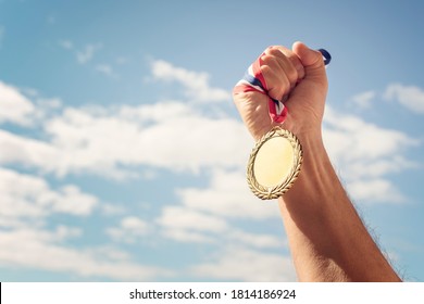 Gold Medal Winner Held In Hand Raised Against Blue Sky Background