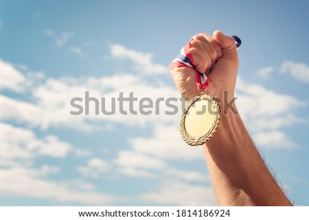 Gold medal winner held in hand raised against blue sky background
