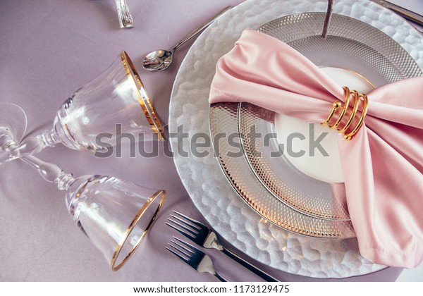 Gold napkin ring on an elegant dinner table with\
flowers and glasses