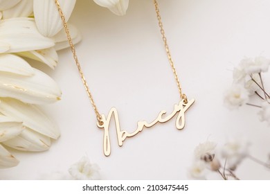 Gold necklace with name inscription displayed on a floral background. Jewelry photo for e-commerce, online sale, social media. - Shutterstock ID 2103475445