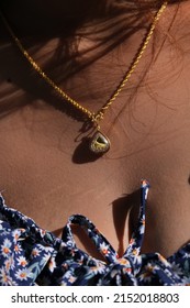 A gold necklace and a pendant, depicting the Lord Buddha (in this case symbolizing Tuesday), worn by a young tanned woman with summer dress