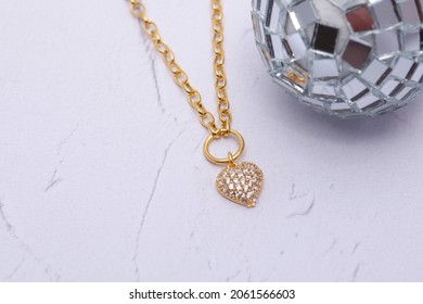 Gold Necklace And Tiny Disco Balls On A White Plate On A Soft White Background.