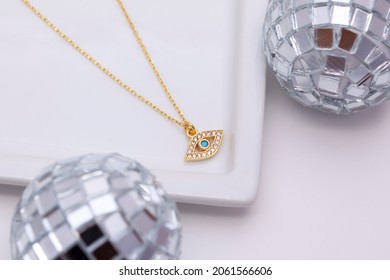 Gold Necklace And Tiny Disco Balls On A White Plate On A Soft White Background.