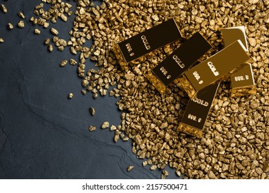 Gold nuggets and ingots on black table, flat lay. Space for text