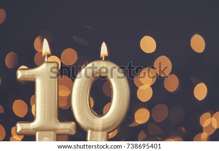 Gold number 10 celebration candle against blurred light background