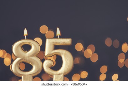Gold number 85 celebration candle against blurred light background