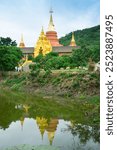 Gold pagoda near the mountain with lake and reflection at big bronze statue , The mock-up Daibutsu Buddha statue and sunlight  at the Wat Doi Phra Chan Buddhist temple of Mae Tha in Lampang ,Thailand.