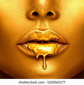 Gold Paint drips from the lips, lipgloss dripping from sexy lips, golden liquid drops on beautiful model girl's mouth, gold metallic skin make-up. Beauty woman face makeup close up. 