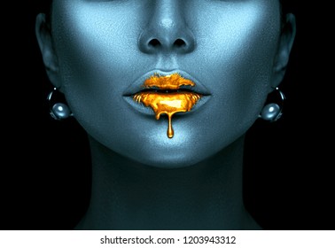 Gold Paint drips from the lips, lipgloss dripping from sexy lips, golden liquid drops on beautiful model girl's mouth, creative abstract dark blue skin make-up. Beauty woman face makeup close up. 