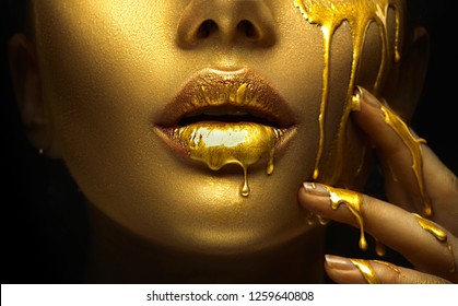 Gold Paint 污迹从脸部、嘴唇和手上滴下来，唇彩从性感的嘴唇上滴下来，金色液体滴在漂亮的模特女孩的嘴上，金色金属皮肤彩妆。美丽的女人化妆关闭。